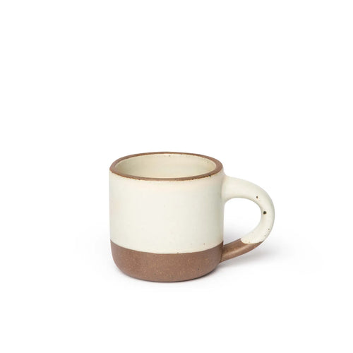 A small sized ceramic mug with handle in a warm off-white glaze featuring iron speckles and unglazed rim and bottom base.