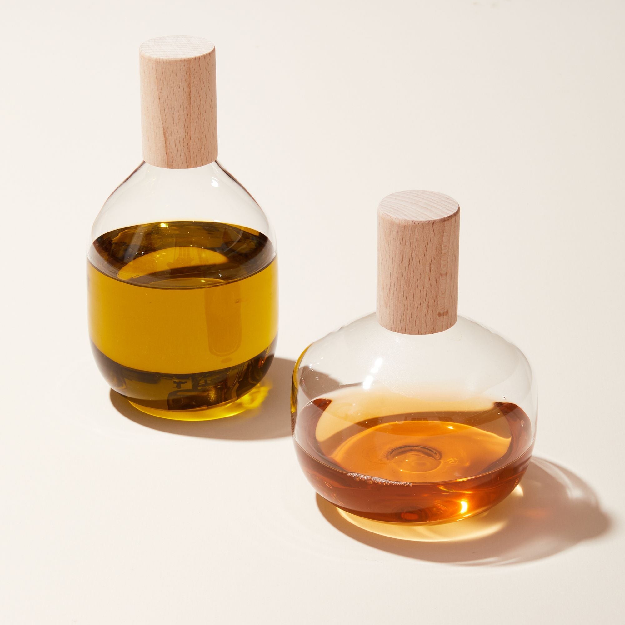 A tall and short glass bottle with wide bodies that hold oil and vinegar with a wood cylindrical top.