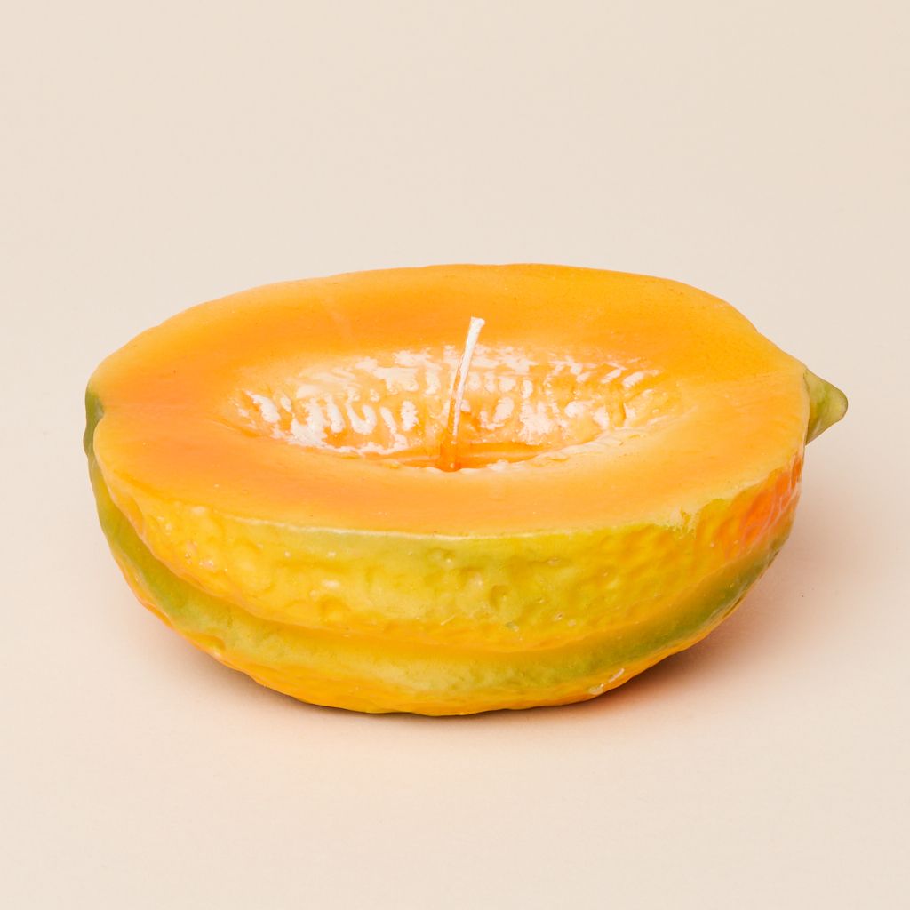 An oblong candle that is light orange with white and green accents, made to suggest a cut-in-half cantaloupe