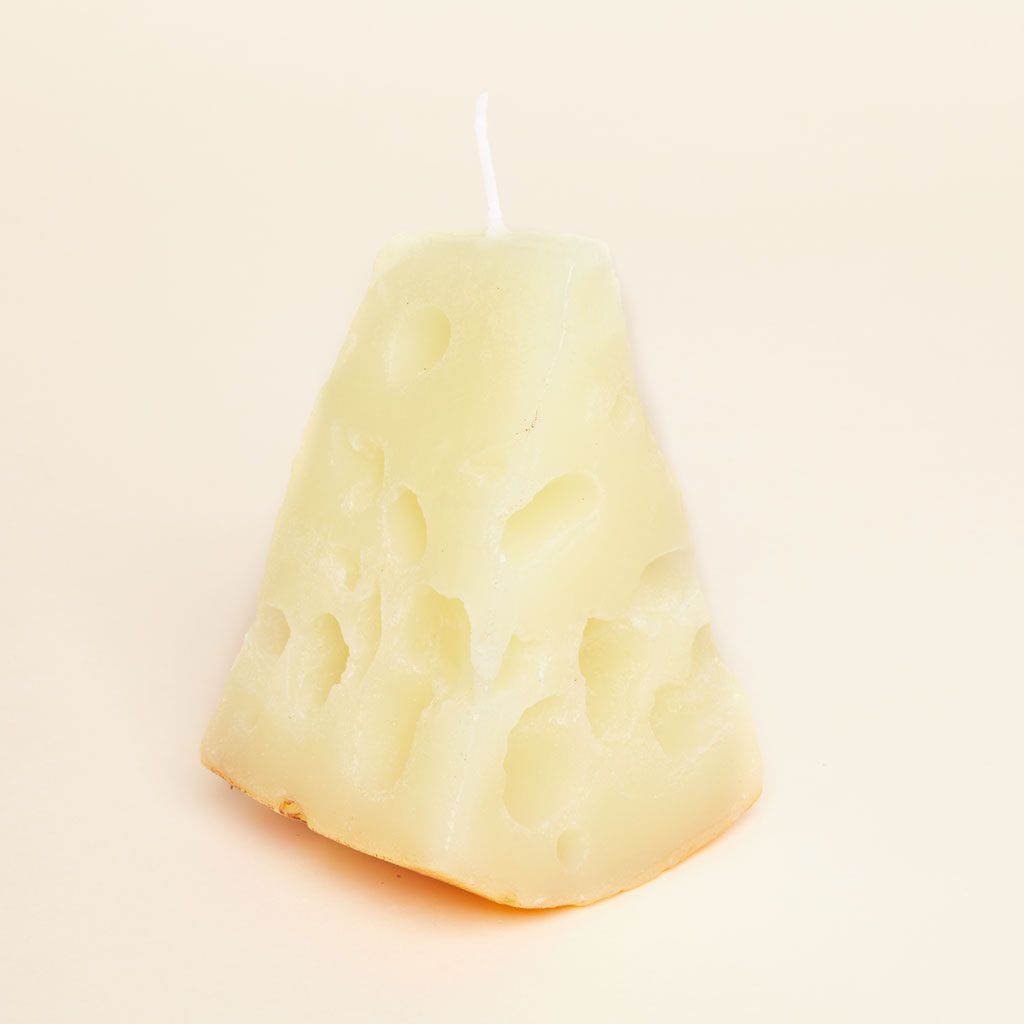 A triangular candle, stood on end, in pale yellow with holes made to resemble a wedge of gruyere cheese