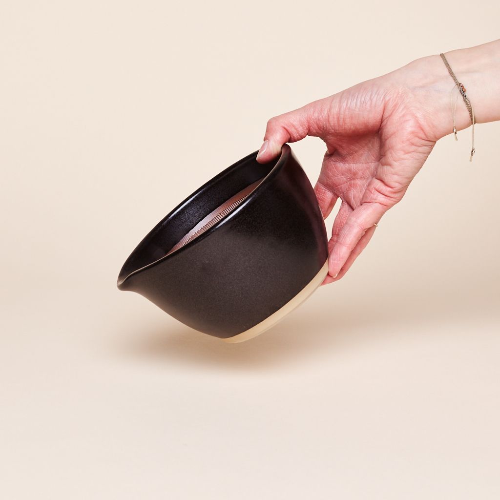 Black bowl-like mortar held at an angle by a hand