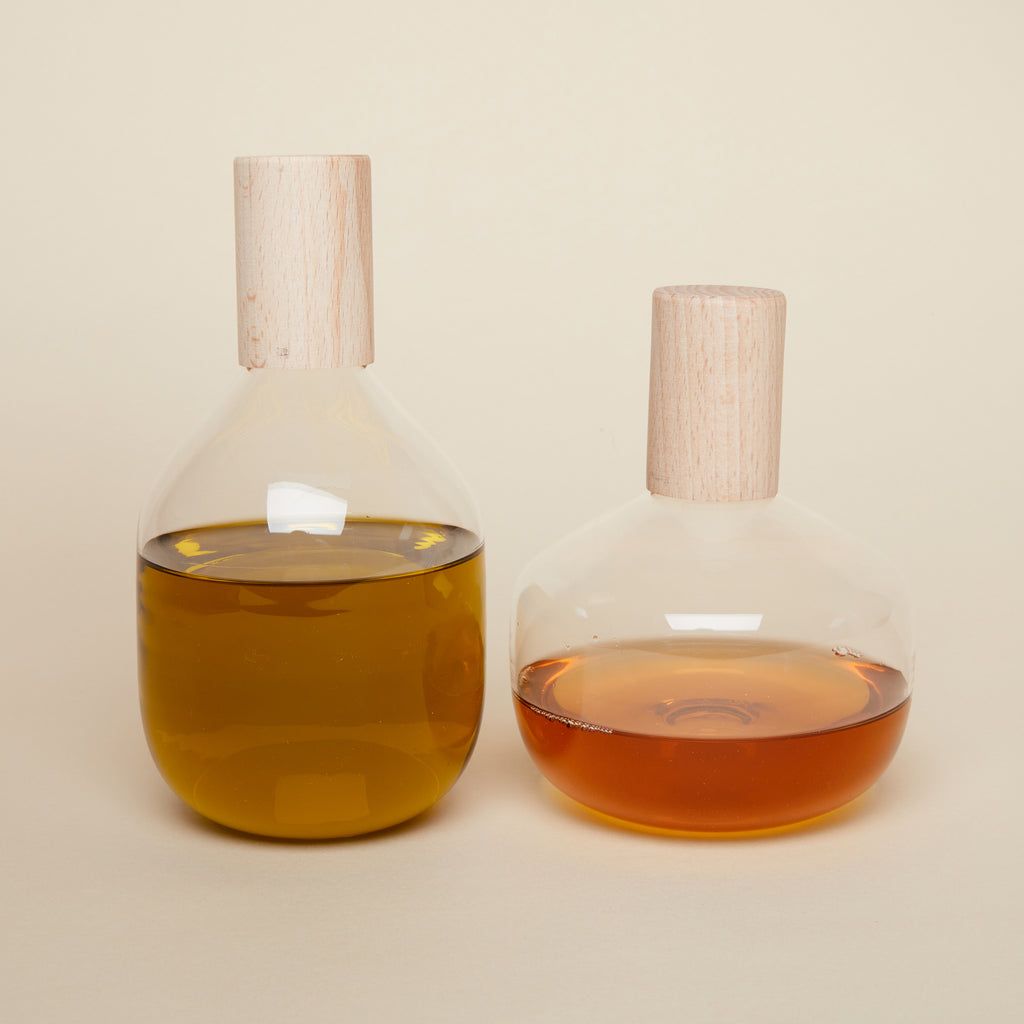 A tall and short glass bottle with wide bodies that hold oil and vinegar with a wood cylindrical top.